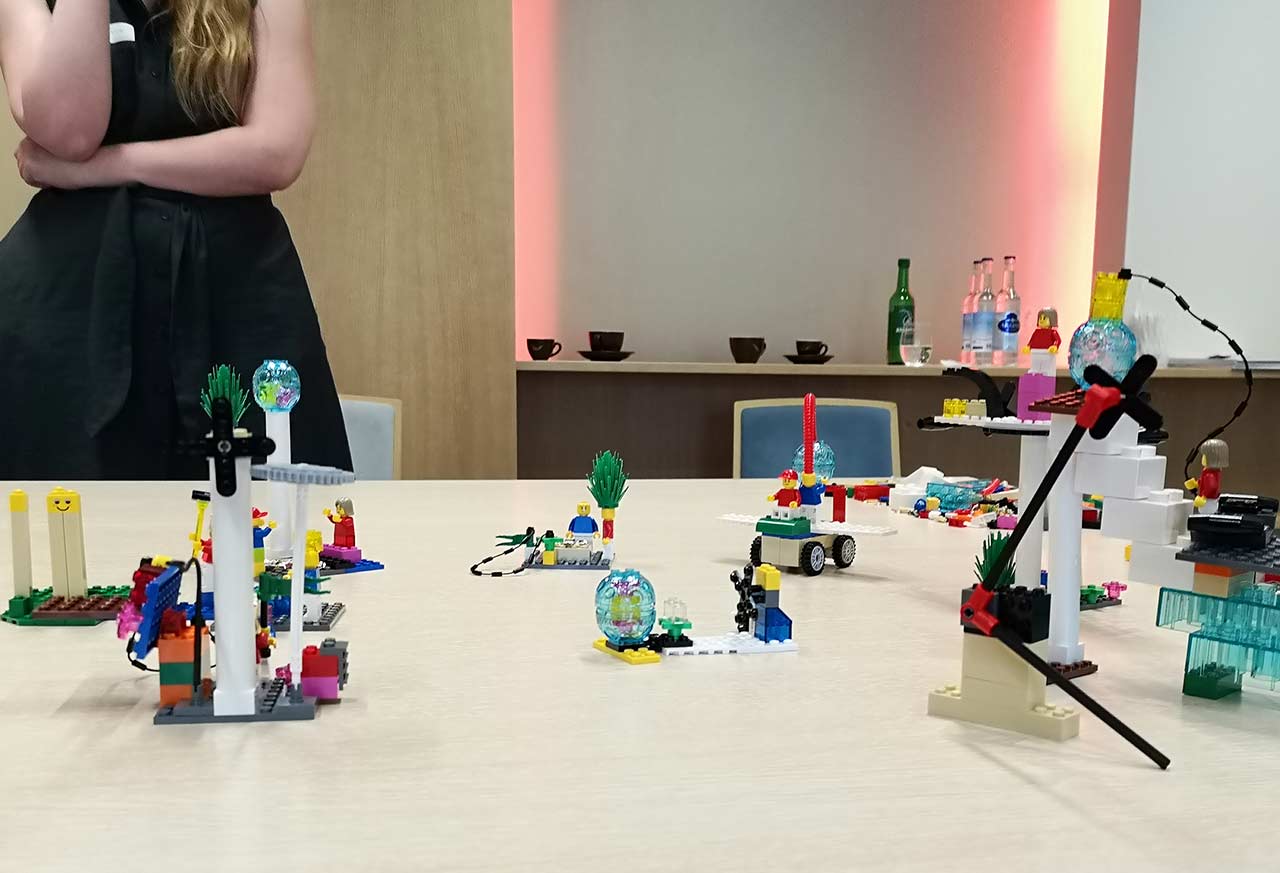 Lego Serious Play Bausteine und Figuren auf dem Tisch mit Frau im Hintergrund